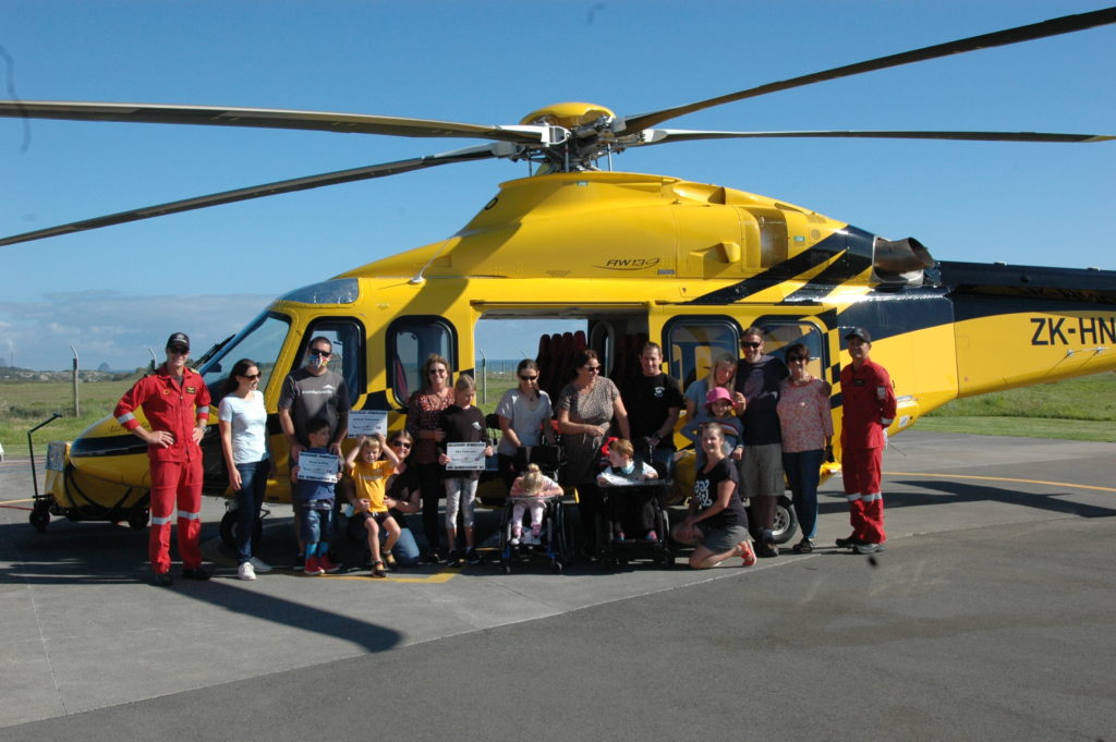 PHI team standing in front of a PHI-branded helicopter with children and their family members from Conductive Education Taranaki.