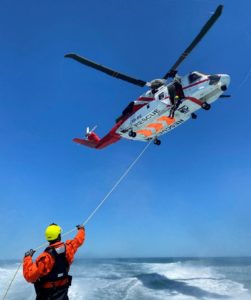 Search and Rescue (SAR) crew member winch training and hoisting another crew person from PHI red and white SAR helicopter