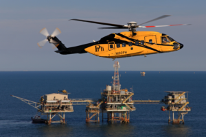 PHI yellow and black S-92 helicopter flying offshore in front of oil and gas rig