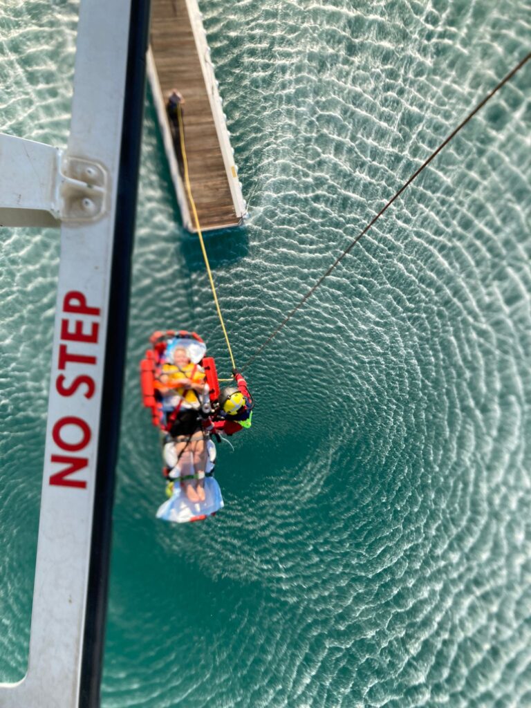 Aerial view of injured persons being winched to safety on helicopter over offshore waters