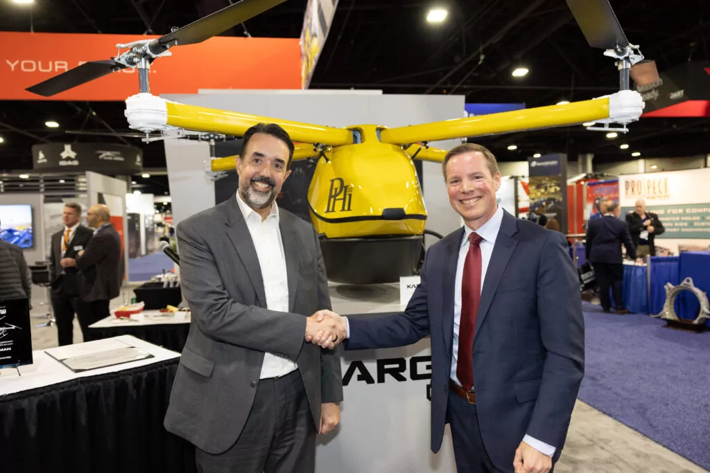 Carroll Lane, President of the Kaman Precision Products Segment, and PHI Aviation - Managing Director Keith Mullett shaking hands in front of half-scale model of KARGO UAV system