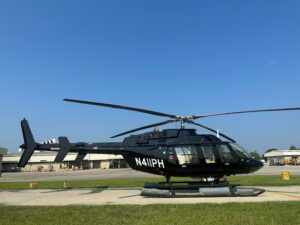 Bell 4017 helicopter painted black sits on the flight line outside with a blue sky