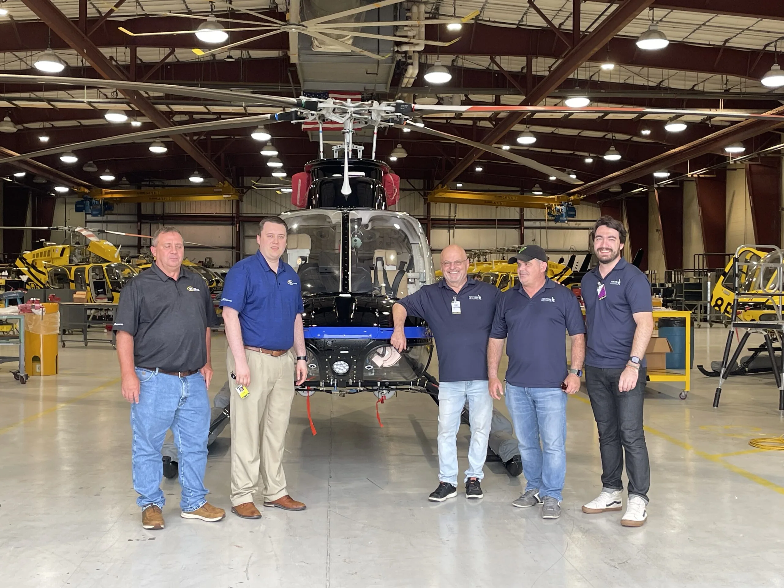 Members of PHI MRO Services and NY Helicopter teams stand in front of black and blue painted Bell407 helicopter