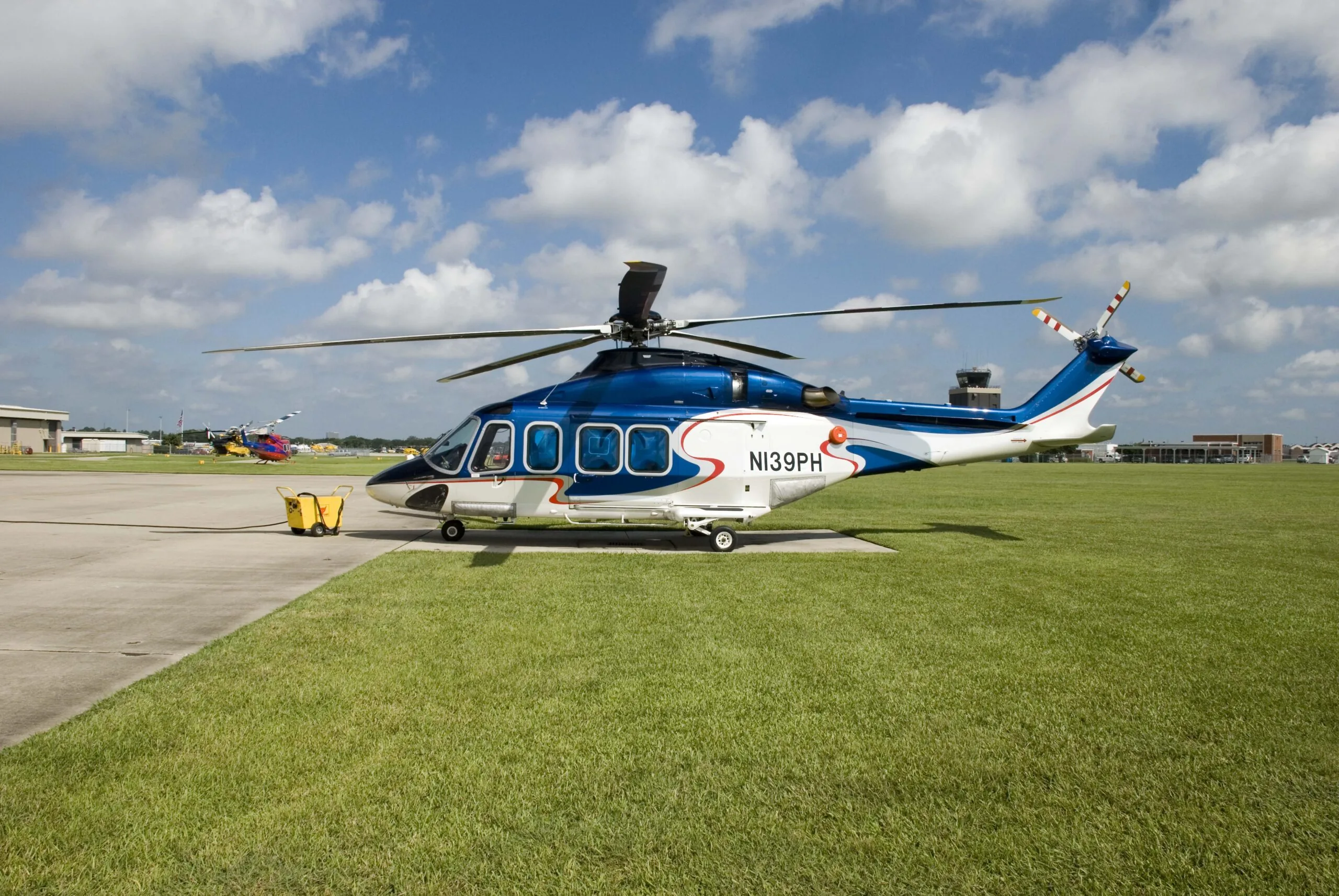 Leonardo AW139 aircraft painted blue with white and red design parked outside with blue sky and green grass